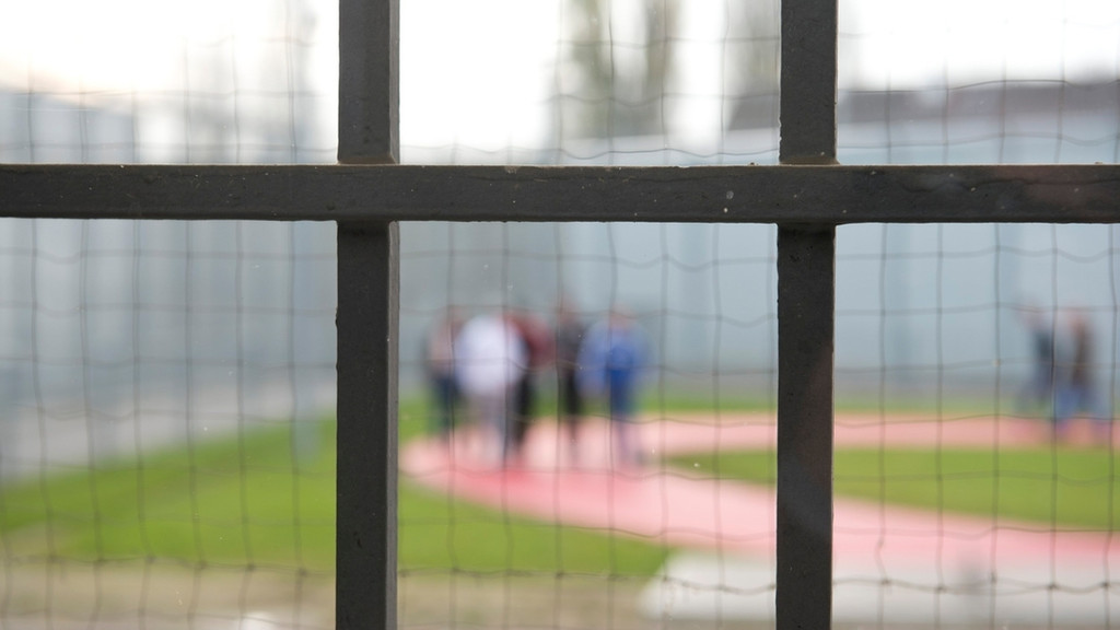 Hinter einem Gitter laufen Gefängnisinsassen 