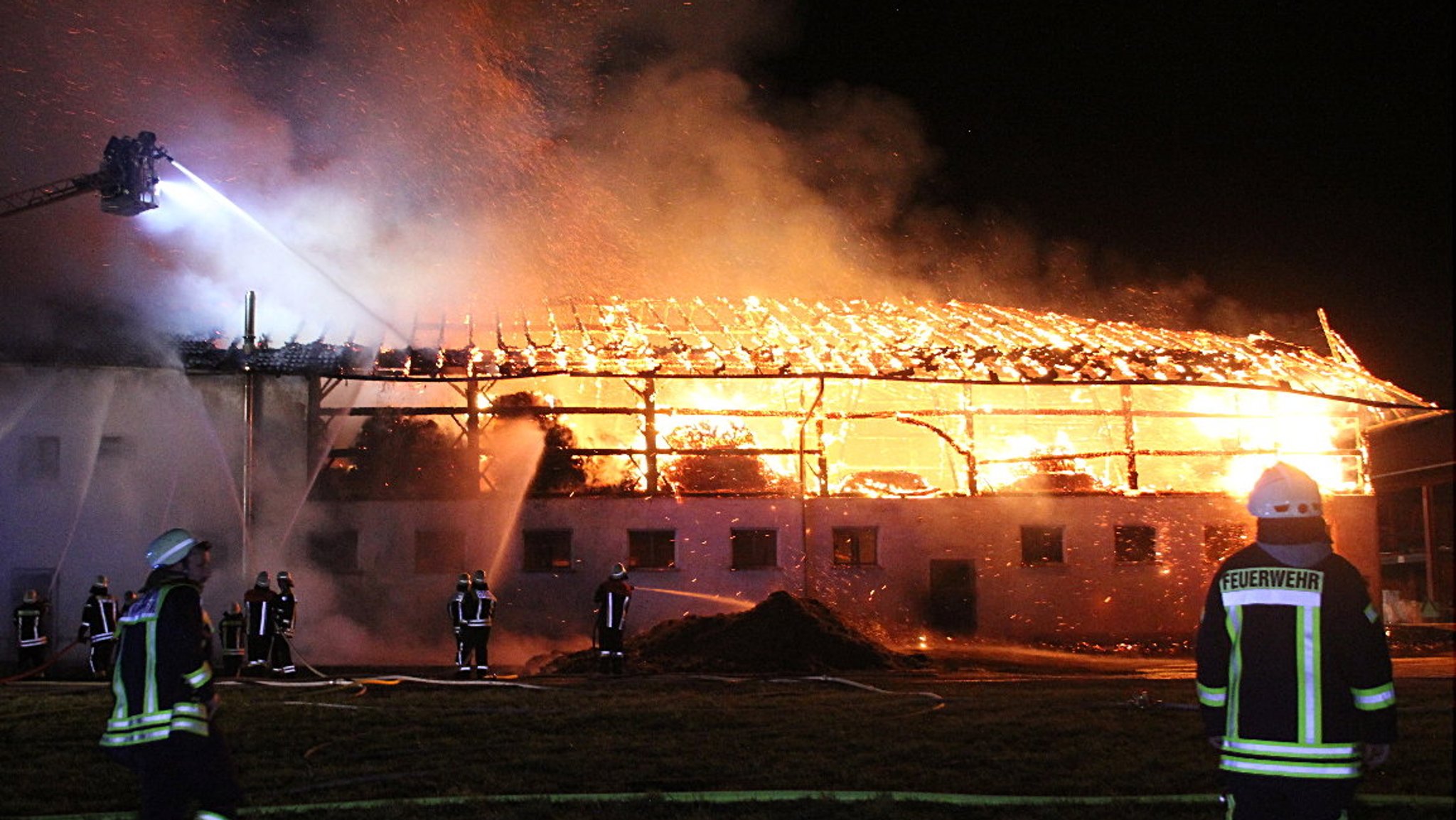 Feuerwehrleute vor der großen brennenden Scheune eines Bauernhofes.