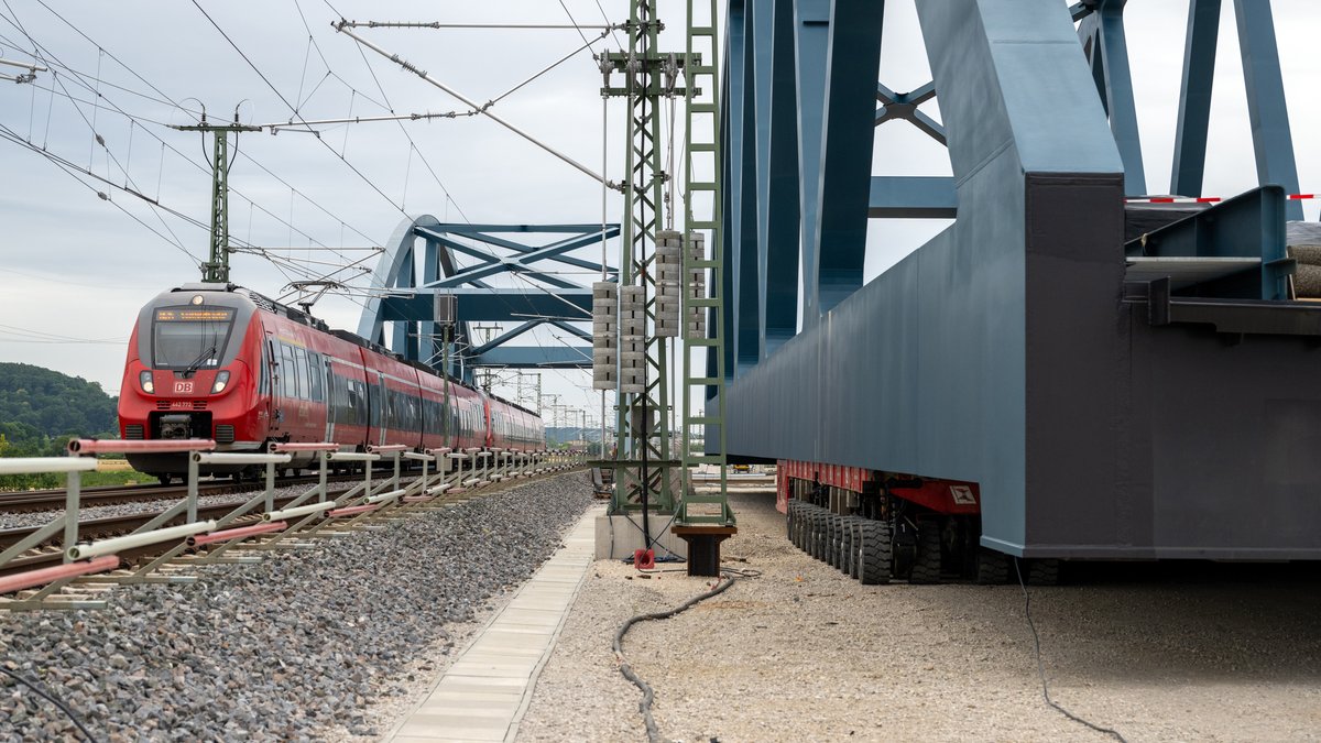 Ein Zug fährt über eine Brücke, während eine identische Zugbrücke daneben auf die Montage wartet. 