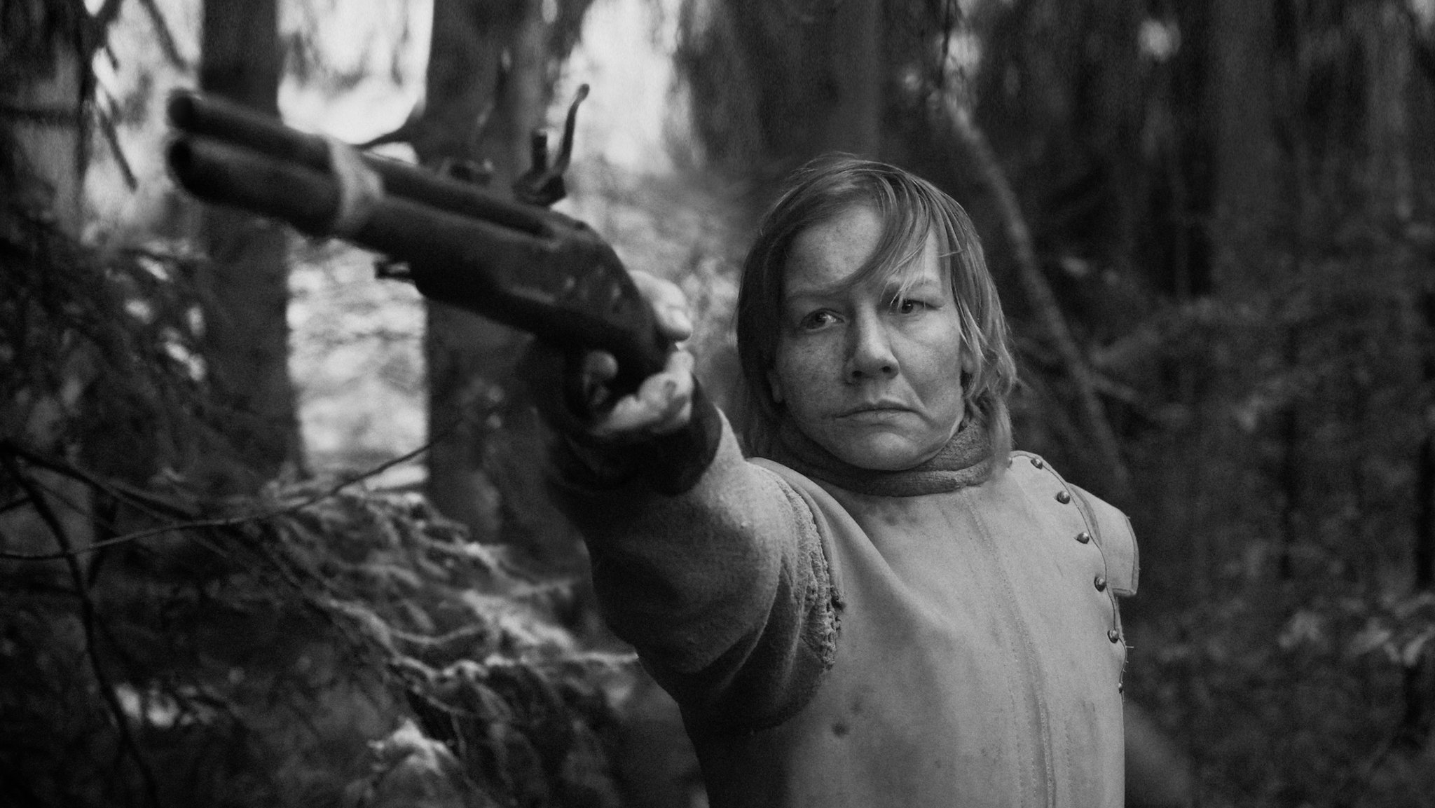 Filmausschnitt: Schwarz-Weiß-Bild einer im Wald stehenden Person, die mit entschlossenem Blick eine Waffe auf ein nicht sichtbares Ziel richtet. | Bild: Schubert, ROW Pictures, Walker+Worm Film, Gerald Kerkletz Filmausschnitt: Schwarz-Weiß-Bild einer im Wald stehenden Person, die mit entschlossenem Blick eine Waffe auf ein nicht sichtbares Ziel richtet.