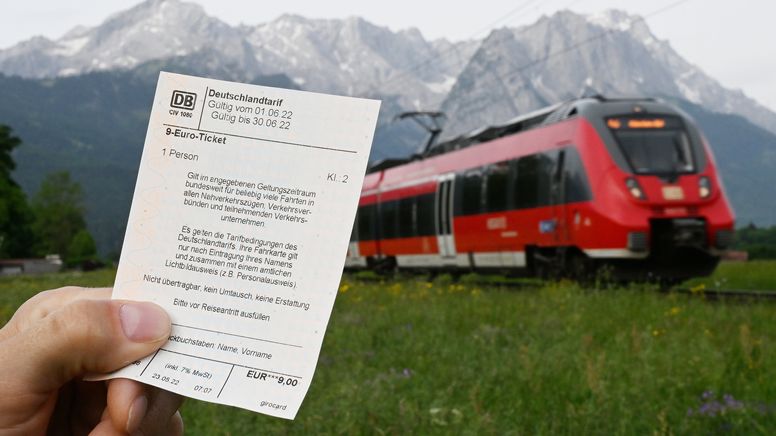 Bayern, Garmisch-Partenkirchen: Ein Mann hält ein 9-Euro-Ticket in der Hand, im Hintergrund fährt ein Zug der Deutschen Bahn vor der Bergkulisse des Wettersteingebirges vorbei  | Bild:dpa-Bildfunk/Angelika Warmuth