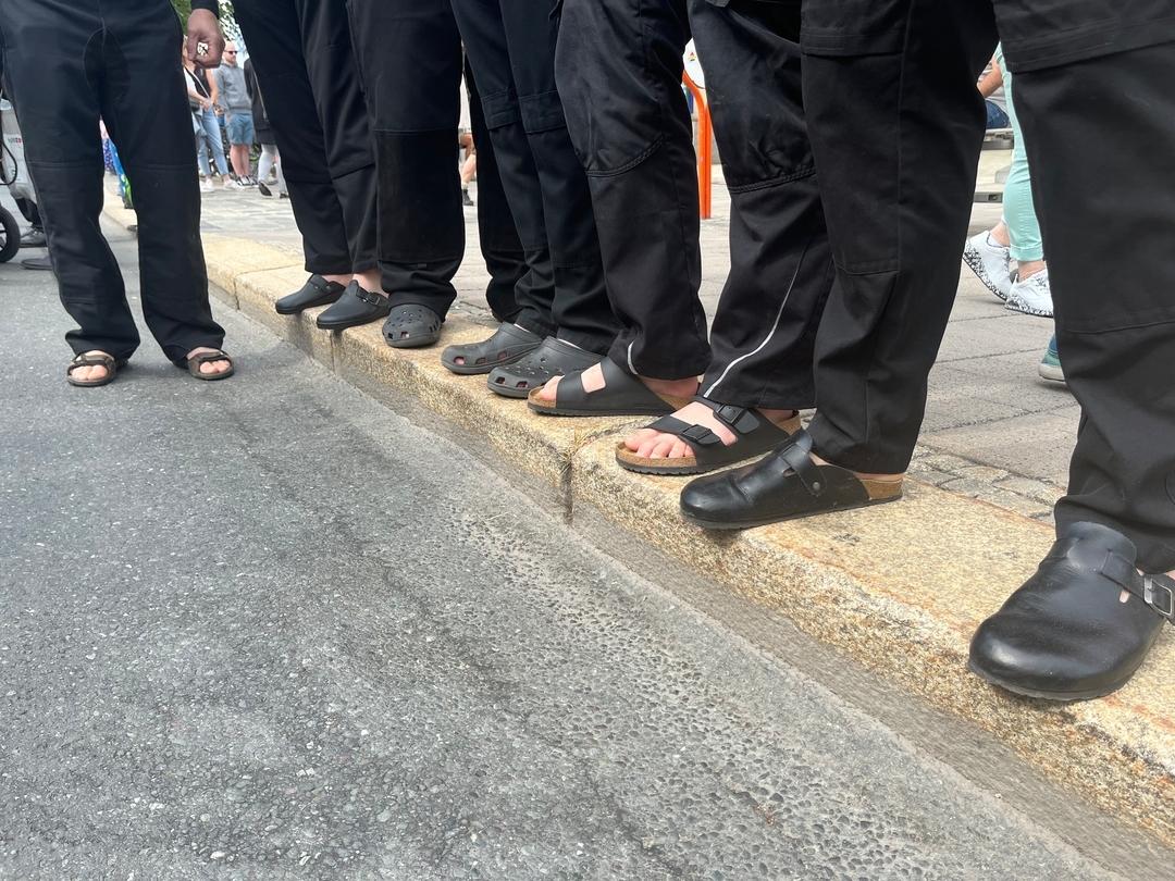 Mehrere Menschen stehen in Hausschuhen auf einem Bürgersteig in Hof.