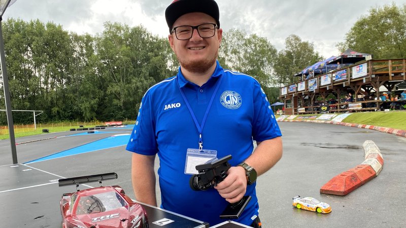 Ein Mann steht mit seinem Modellwagen auf einer Rennstrecke. In der Hand hält er eine Fernsteuerung. | Bild: BR24/Anja Bischof Ein Mann steht mit seinem Modellwagen auf einer Rennstrecke. In der Hand hält er eine Fernsteuerung.