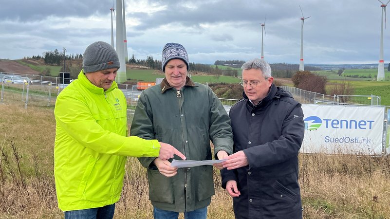 Drei Männer stehen auf einer Süd-Ost-Link-Baustelle und betrachten einen Plan. | Bild: BR/Annerose Zuber Drei Männer stehen auf einer Süd-Ost-Link-Baustelle und betrachten einen Plan.
