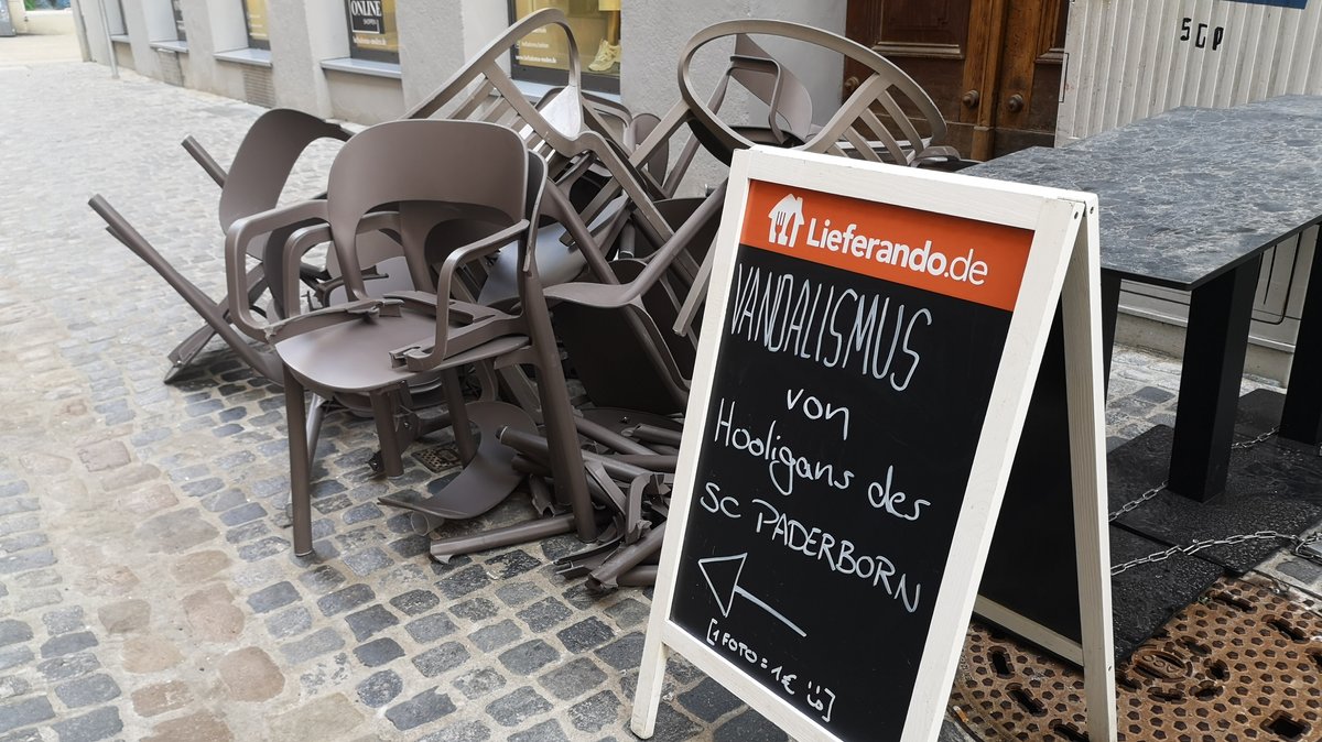 Auf einem Schild vor einem Haufen kaputter Stühle steht: "Vandalismus von Hooligans des SC Paderborn. 1 Foto = 1 Euro)