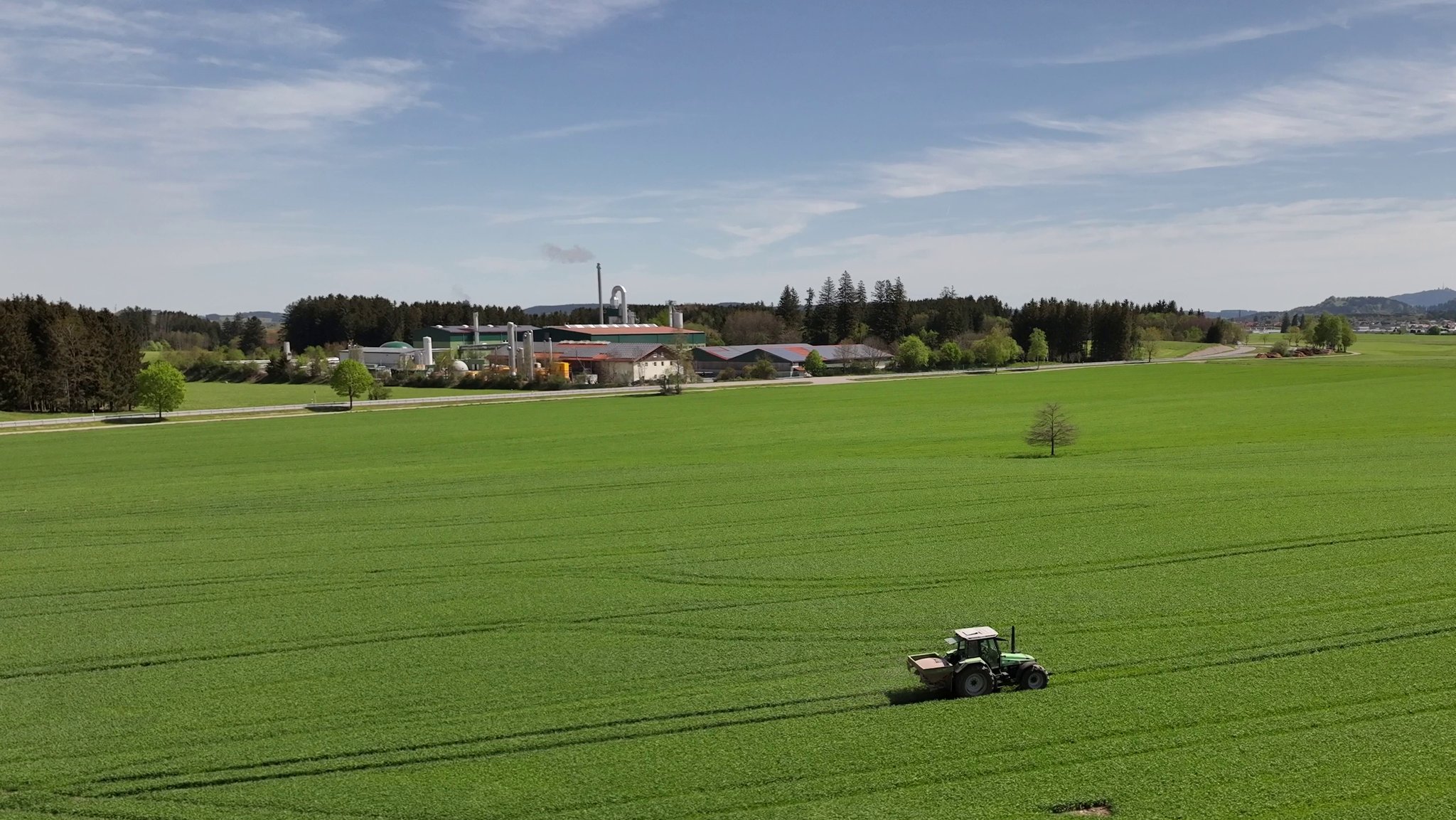 Landwirtschaftliches Feld mit Traktor vor der jetzt in Betrieb genommenen Recyclinganlage.