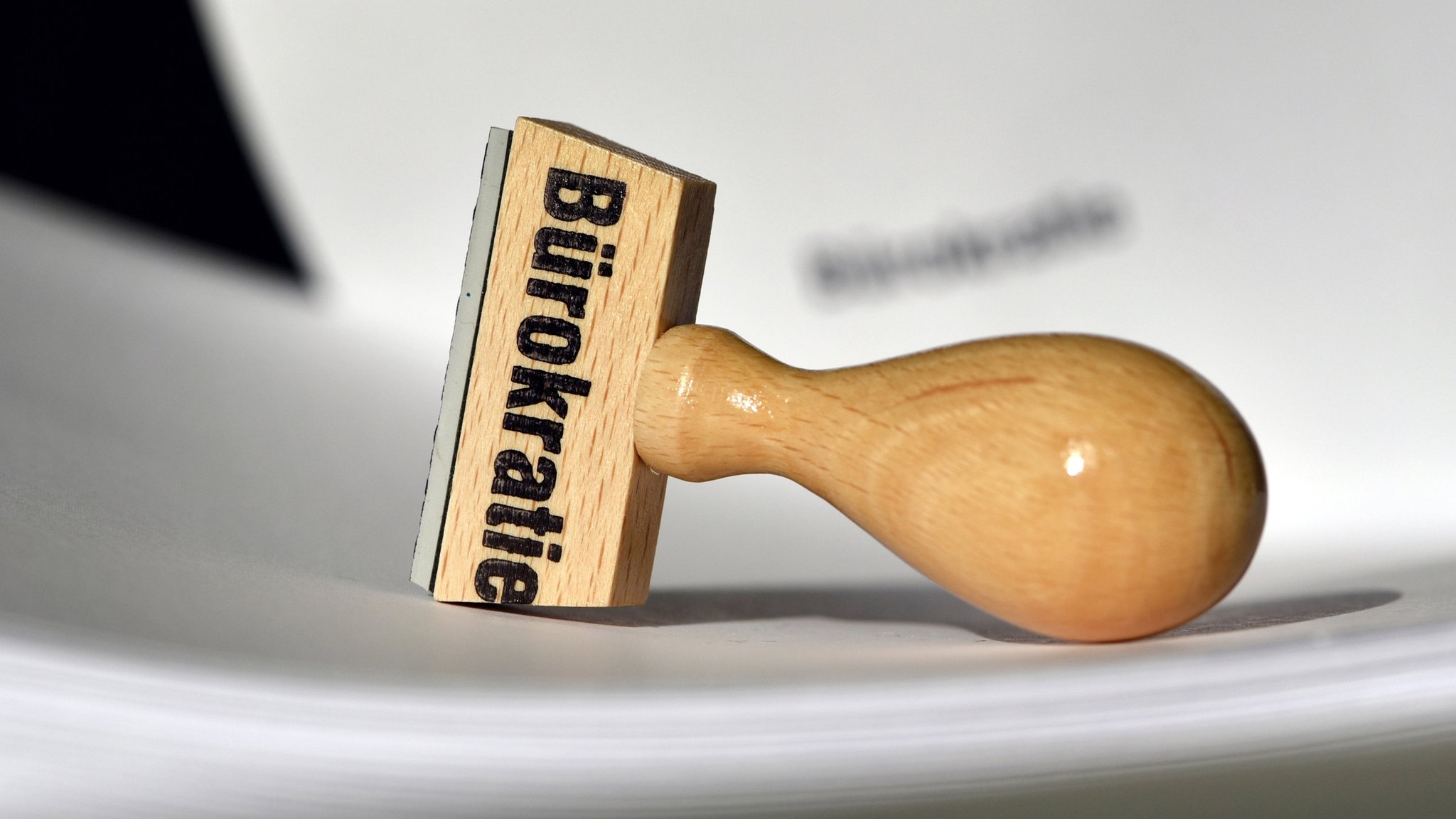 Ein Stempel mit der Aufschrift "Bürokratie" liegt auf Papieren.