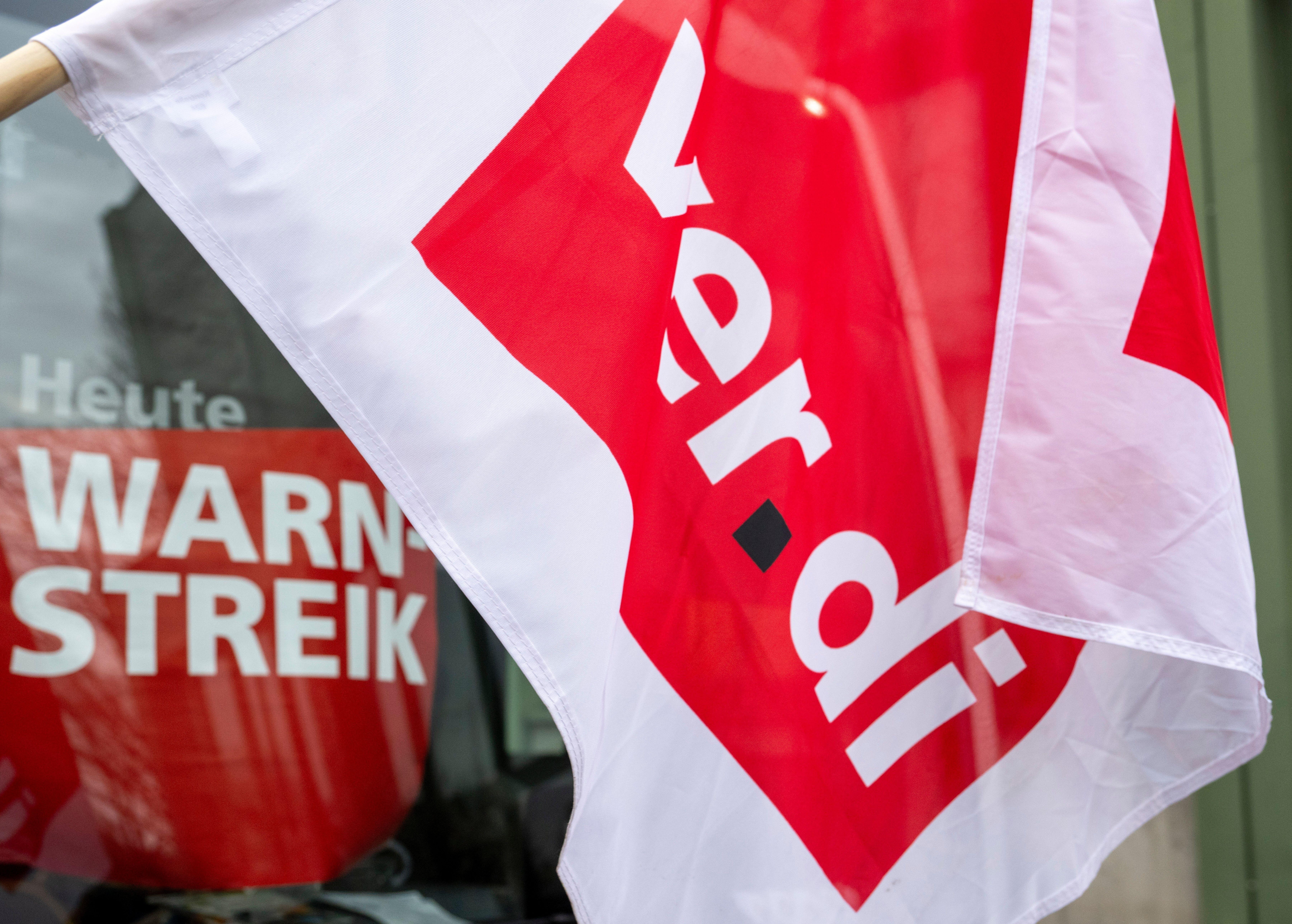 Nahaufnahme einer Verdi-Fahne, dahinter ein Plakat mit der Aufschrift "Heute Warnstreik". Nach den Osterfeiertagen müssen sich Pendler erneut auf Warnstreiks im öffentlichen Nahverkehr einstellen. Laut Verdi sind am Dienstag Augsburg und am Mittwoch Nürnberg betroffen. 