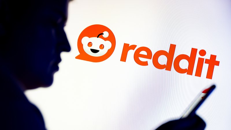 Der Schattenriss eines Mannes, der auf sein Smartphone sieht. Im Hintergrund ist das Reddit-Logo zu sehen. | Bild: picture alliance / ZUMAPRESS.com | Mateusz Slodkowski Der Schattenriss eines Mannes, der auf sein Smartphone sieht. Im Hintergrund ist das Reddit-Logo zu sehen.