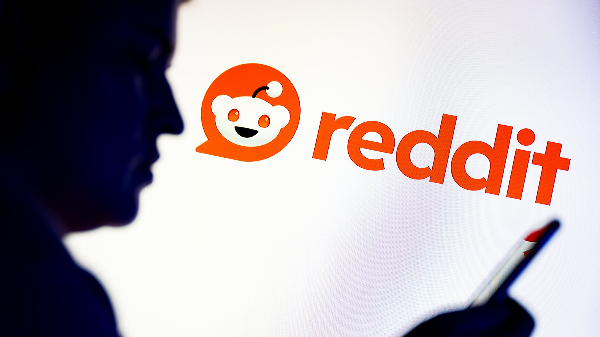 Der Schattenriss eines Mannes, der auf sein Smartphone sieht. Im Hintergrund ist das Reddit-Logo zu sehen.