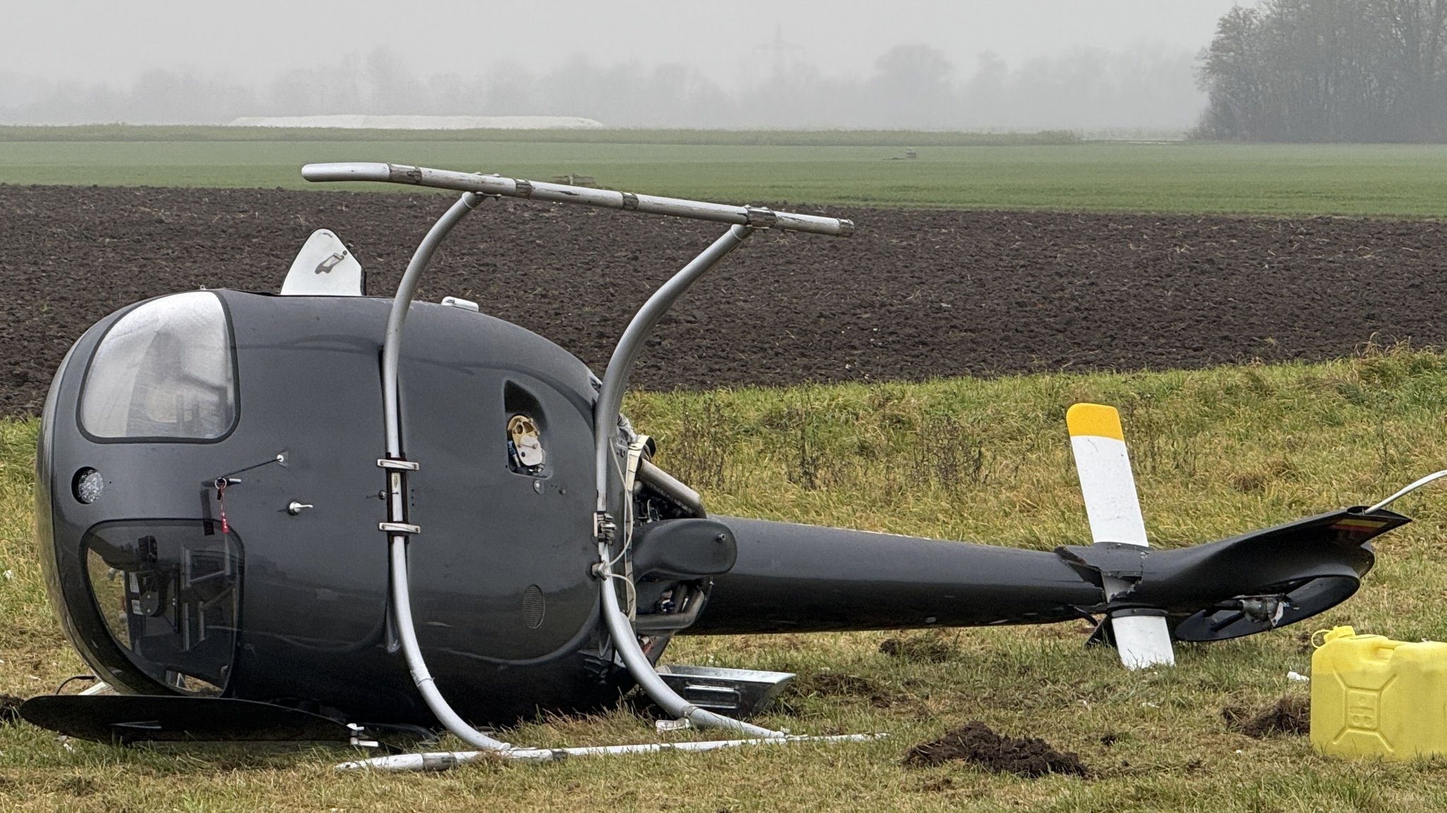 Ein abgestürzter Hubschrauber liegt auf der Seite auf einer Wiese.