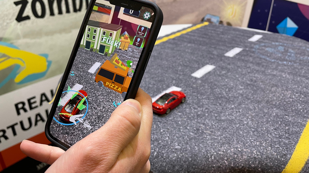 Ein Spielzeugauto auf einer Straßenmatte, ein Smartphone filmt mit Augmented Reality.