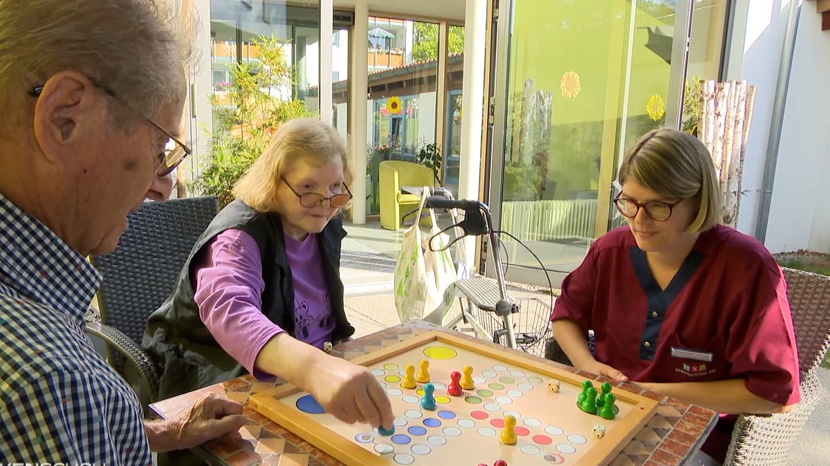 Eine Pflegerin spielt mit zwei Senioren ein Brettspiel.