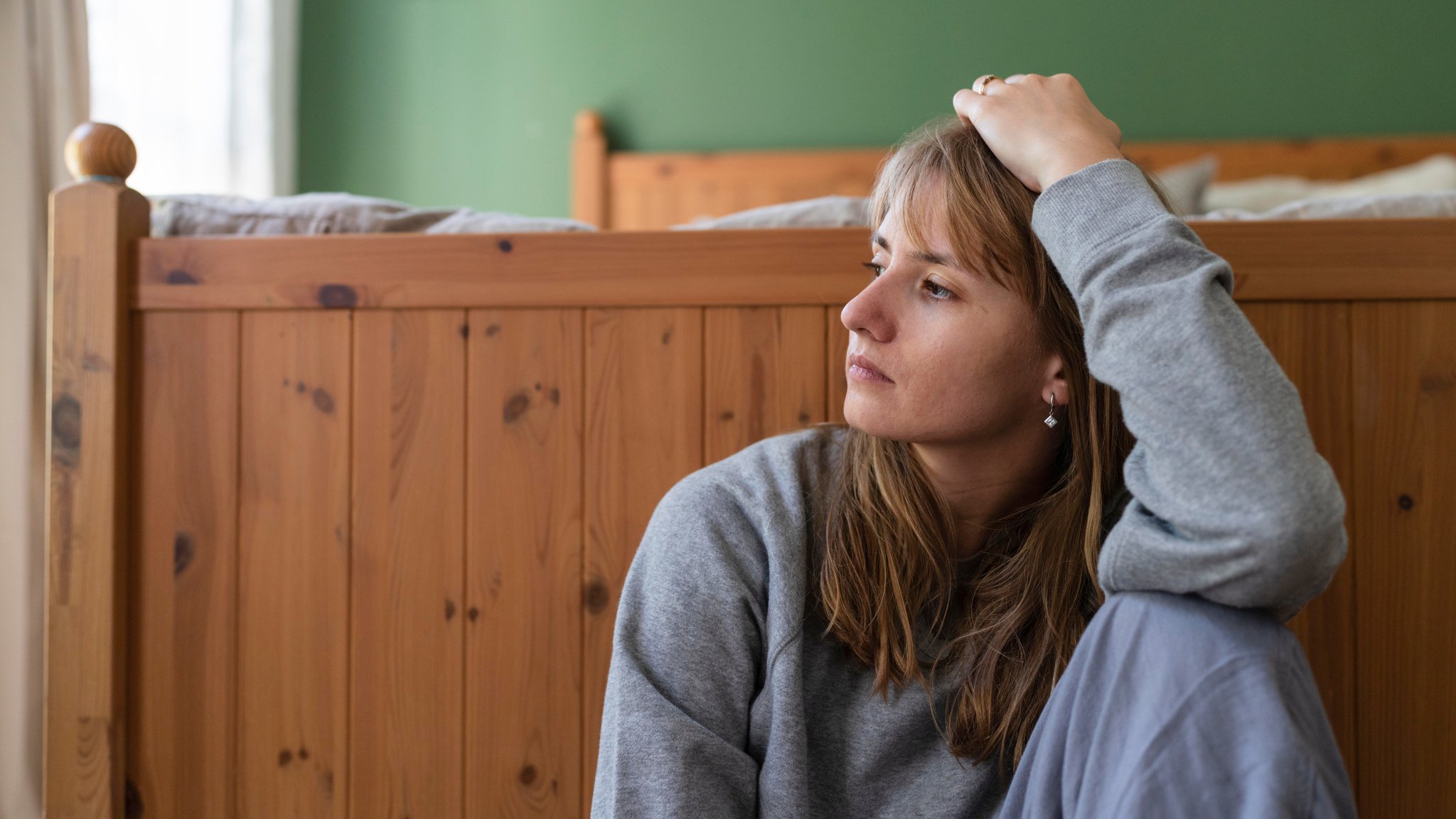 Nachdenklich blickende Frau sitzt vor ihrem Bett