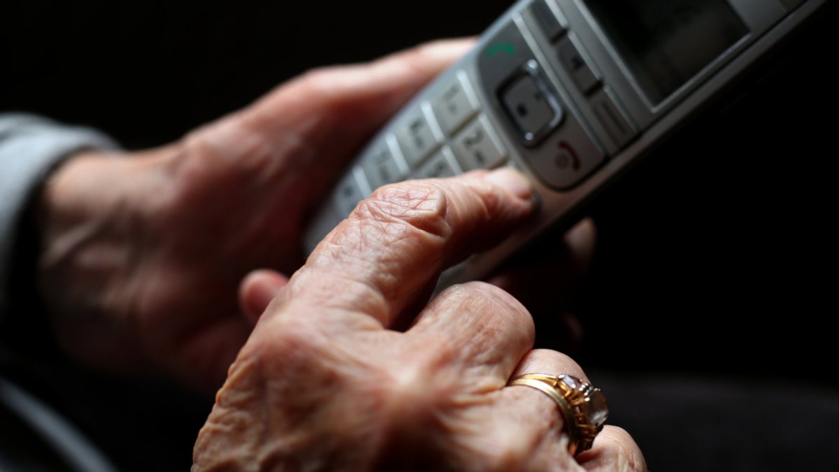 Eine ältere Frau tippt auf einem schnurlosen Festnetztelefon. 