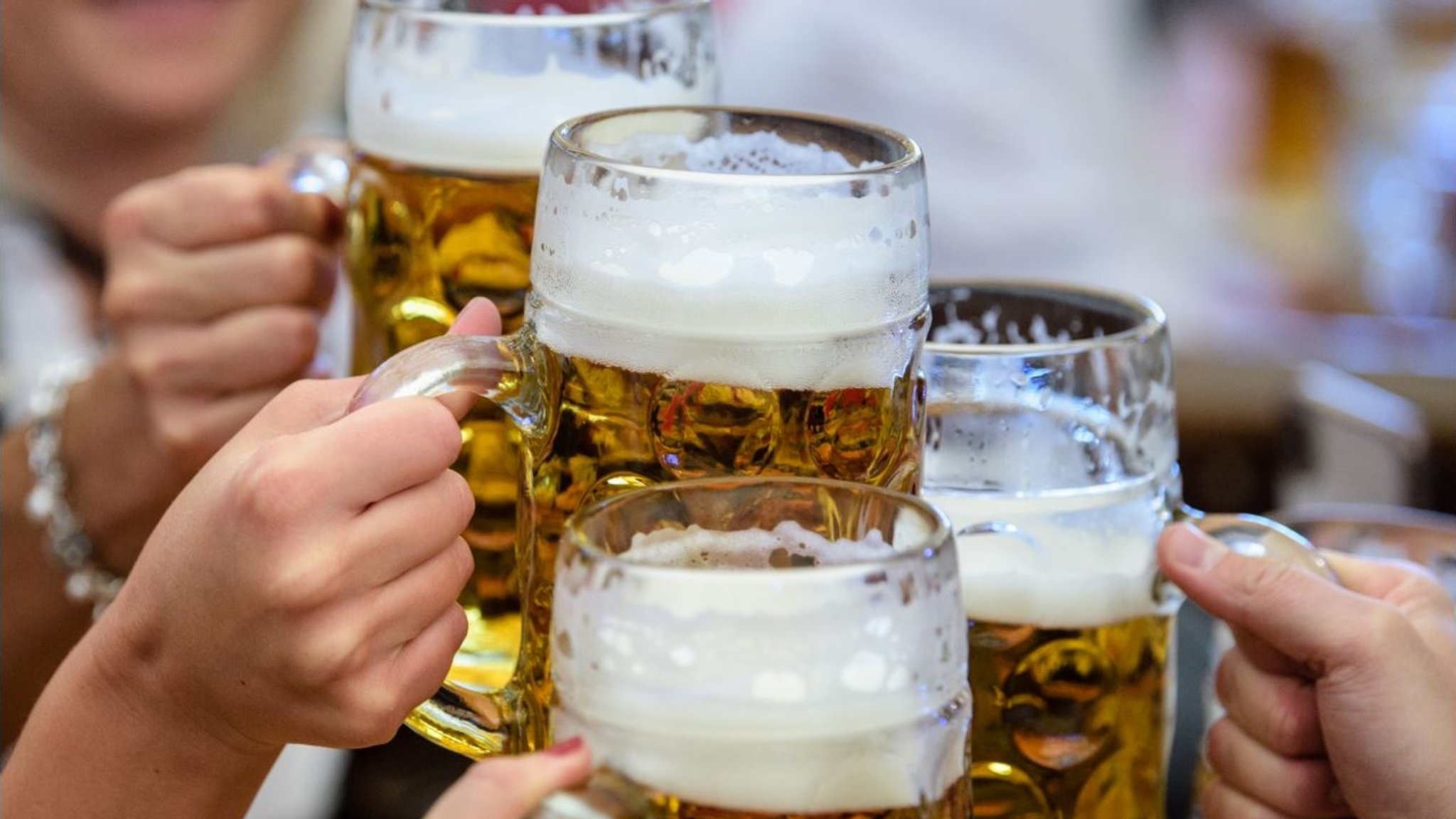 Menschen stoßen mit gefüllten Bierkrügen an (Symbolbild)