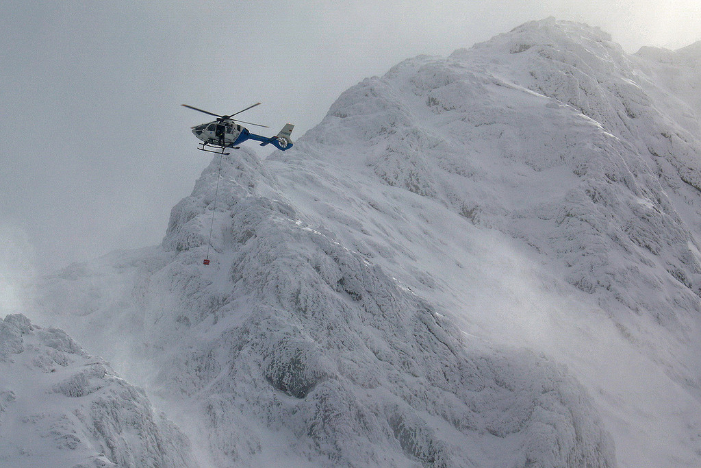 Ein Hubschrauber fliegt mit einem tonnenförmigen Suchgerät am Seil über eine vereiste und verschneite Bergflanke des Hochkalter.