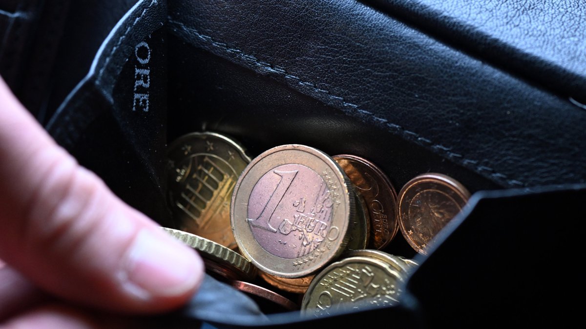 Eine Hand greift in einen Geldbeutel mit Münzen.