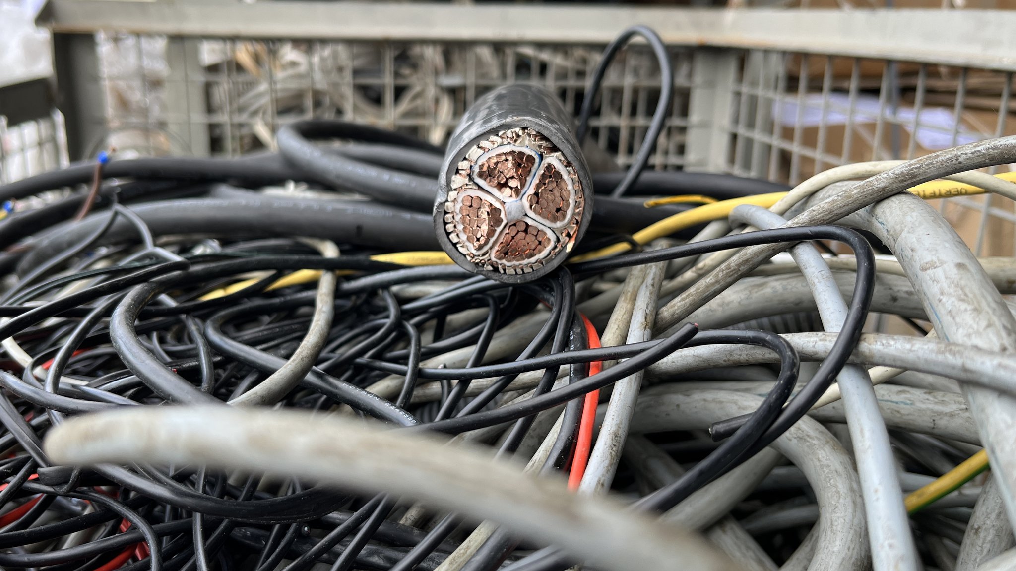 In einer Kiste voller alter Kabel liegt auch ein sehr dickes Kabel, an dessen Querschnitt man viele kleinere Kupferdrähte sieht.