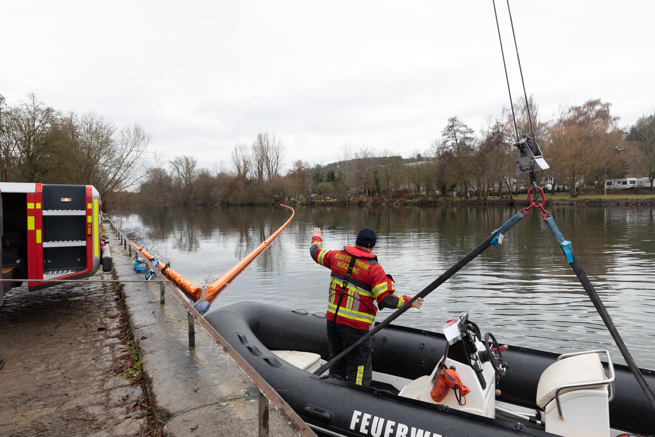 Ein Feuerwehrbot wird auf den Main heruntergelassen, im Hintergrund die Ölsperre quer über den Fluß. 