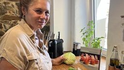 Köchin und Foodstylistin Beate Roth steht mit einem Kohlkopf in der Hand vor einem Schneidbrett in ihrer Küche. | Bild:BR / Annerose Zuber
