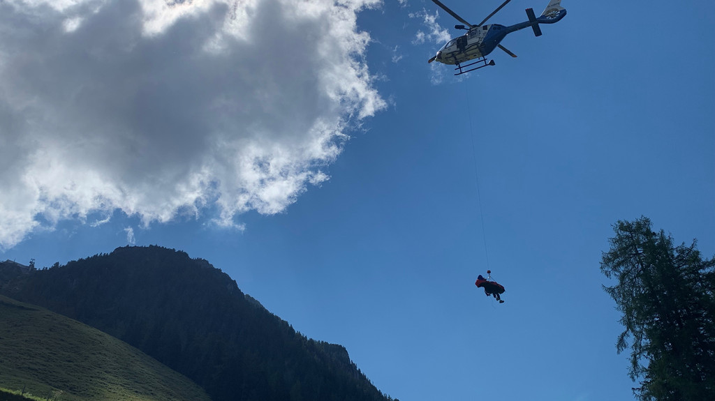 Ein Hubschrauber transportiert einen Bergretter und einen Verletzten.