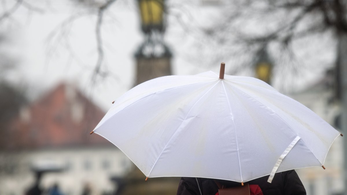 Eine Frau geht mit Regenschirm am Schlosskanal Nymphenburg entlang. 