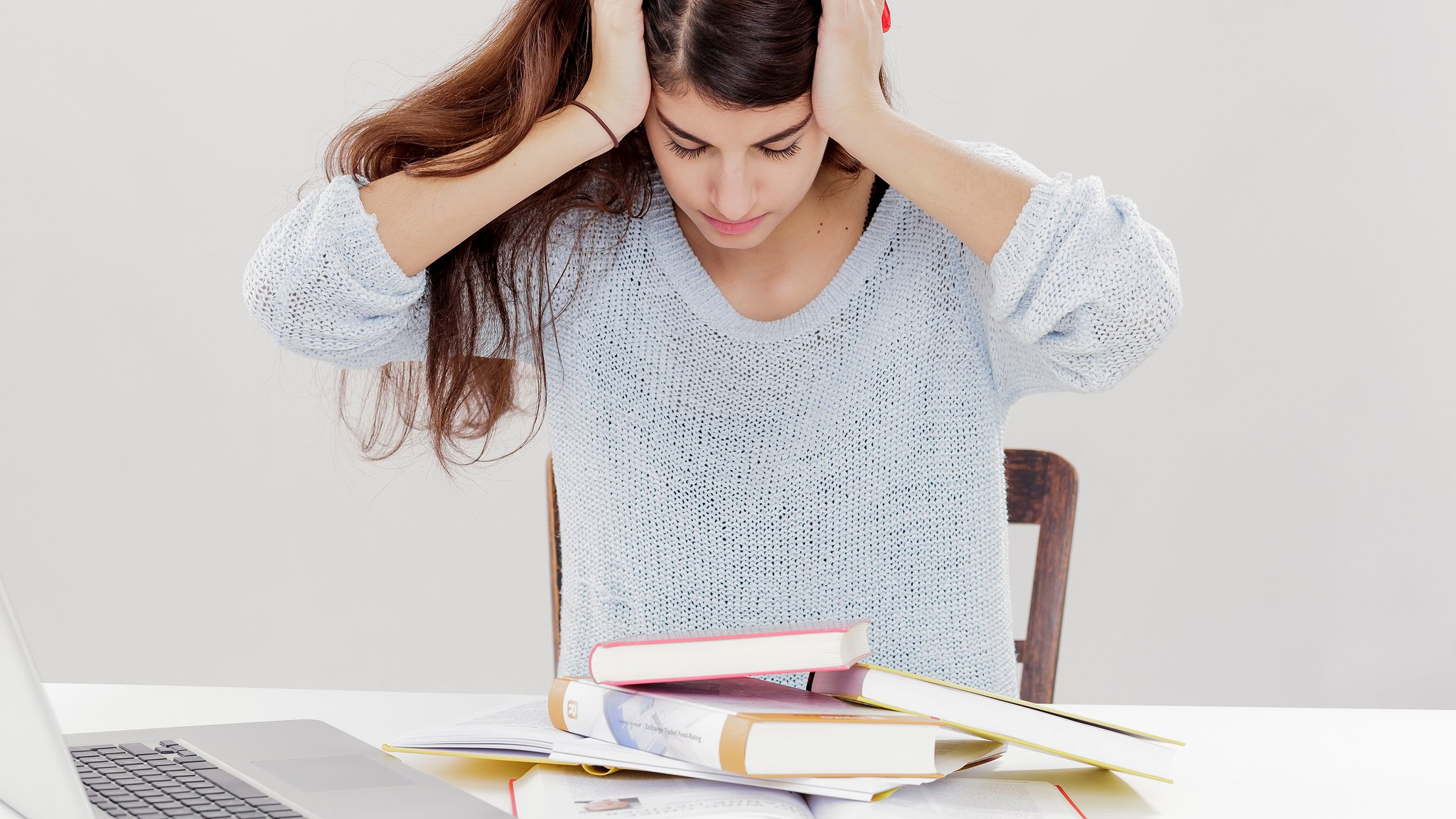 Eine junge Frau sitzt vor ihren Lehrbüchern und ist verzweifelt, weil sie mit dem Lernstoff überfordert ist.