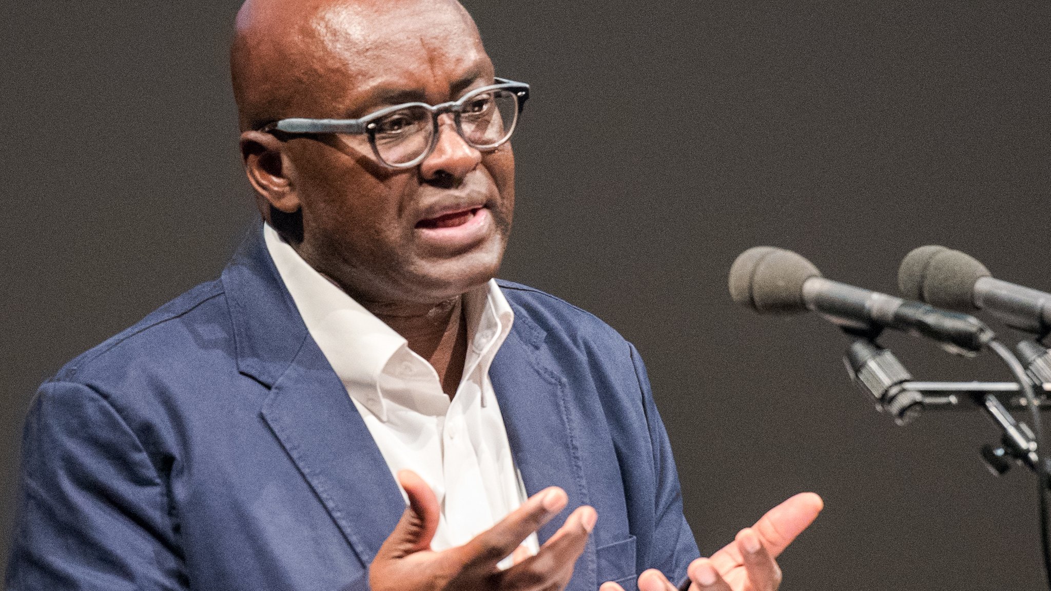 Politikwissenschaftler Achille Mbembe steht an einem Rednerpult mirt zwei Mikrofonen und spricht