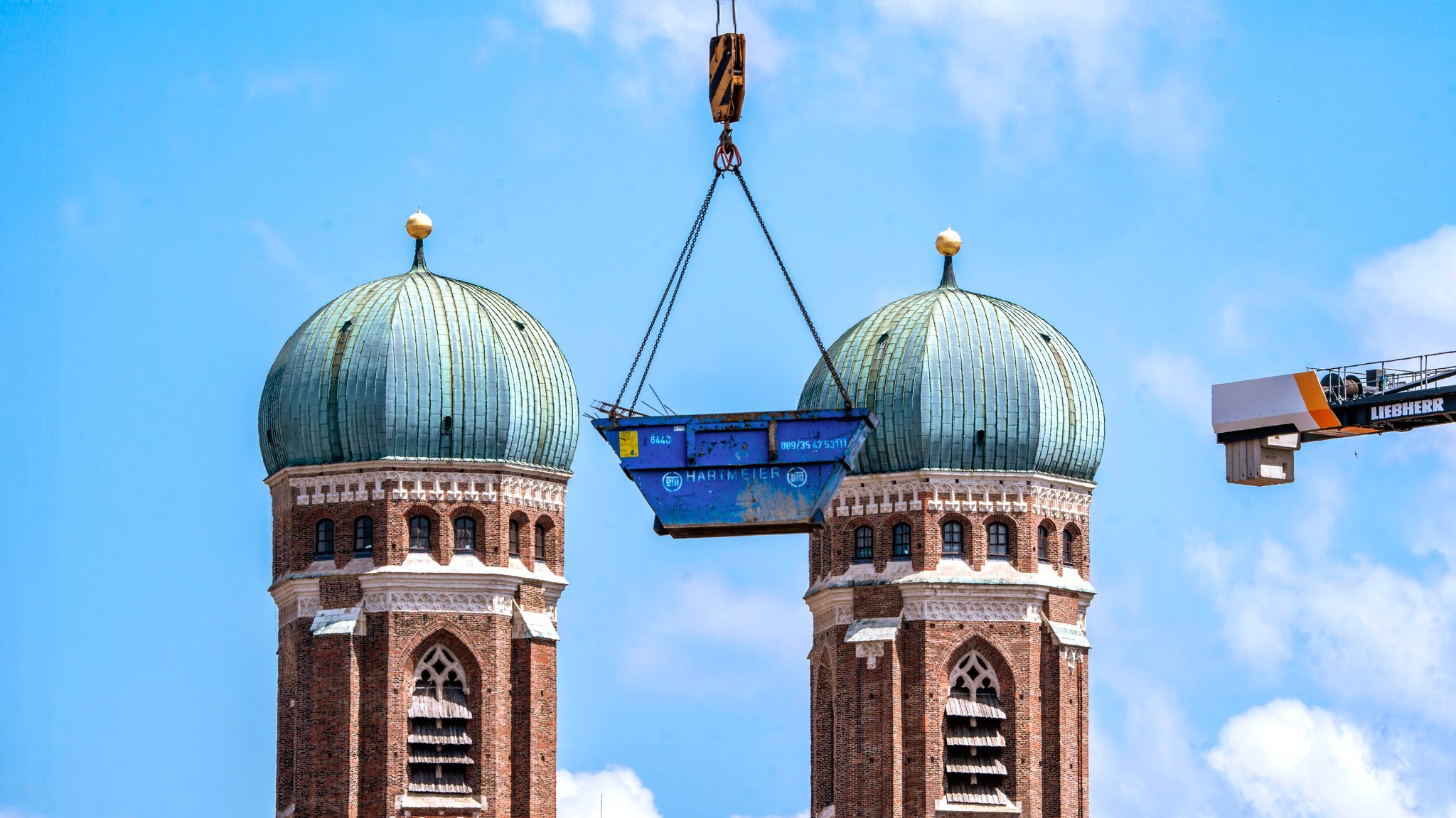 Juni 2024: Ein Baucontainer schwebt an einem Kran vor den Türmen der Münchner Frauenkirche.