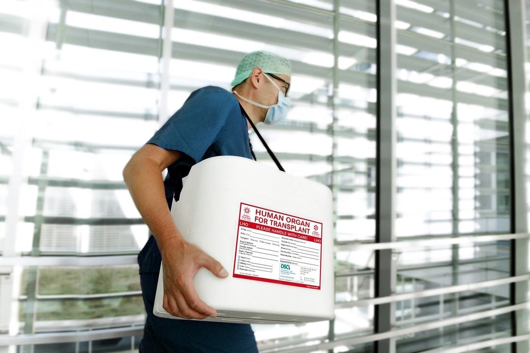 Symbolbild: Ein Mann mit Mundschutz trägt einen Container für den Organtransport