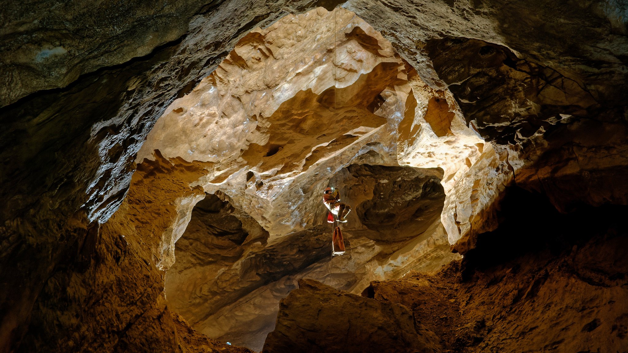 Ein Höhlenforscher seilt sich freischwebend an einem Seil in einen großen Schacht in einer zerklüfteten Felshöhle ab