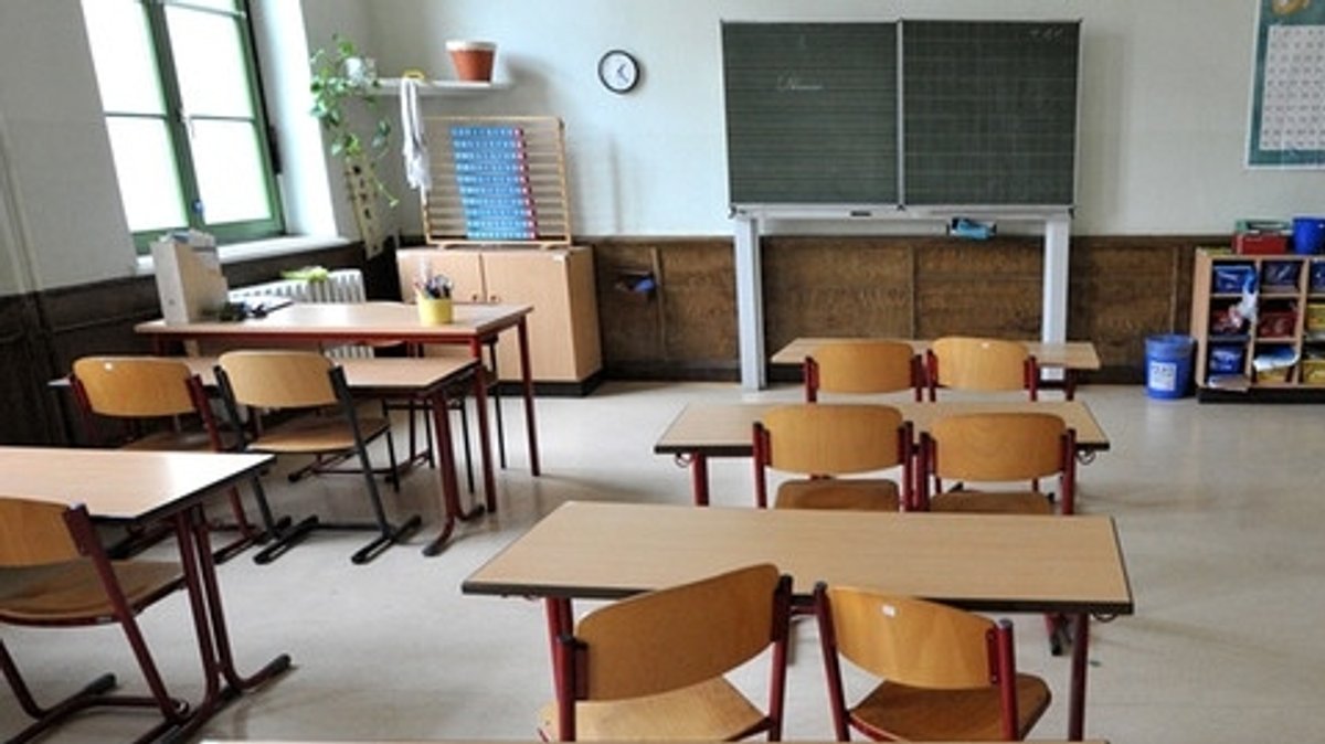 Ein Klassenzimmer mit Tischen und Stühlen, an der Wand ein Tafel. 