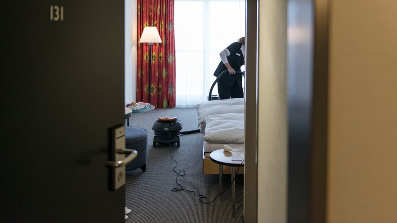 Ein Zimmermädchen beim Staubsaugen im Zimmer. | Bild: picture alliance/KEYSTONE | CHRISTIAN BEUTLER Ein Zimmermädchen beim Staubsaugen im Zimmer.