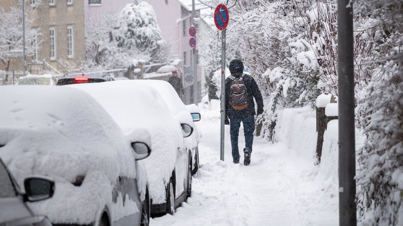 Eine Person geht auf einem verschneiten Gehweg entlang. Die parkenden Autos sind mit Schnee bedeckt. Im Verlauf des Tages gibt es weitere Schneefälle und Glätte. (26.01.2026) | Bild: picture alliance/dpa | Daniel Vogl Eine Person geht auf einem verschneiten Gehweg entlang. Die parkenden Autos sind mit Schnee bedeckt. Im Verlauf des Tages gibt es weitere Schneefälle und Glätte. (26.01.2026)