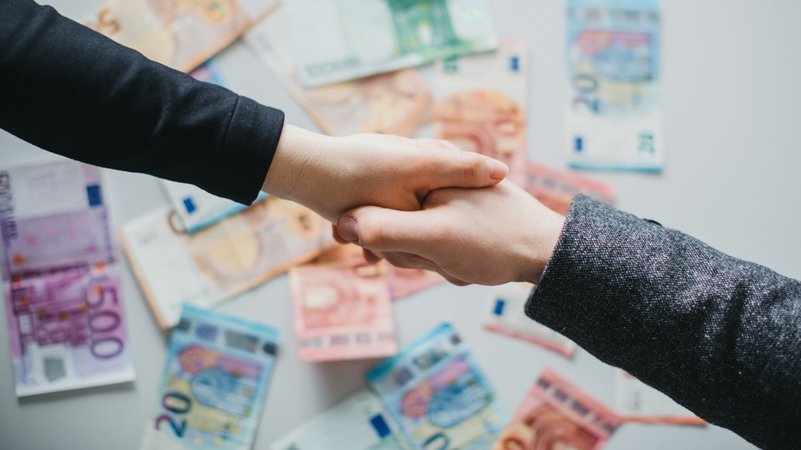 Hand geben zum Vertragsabschluss. Geldscheine im Hintergrund. | Bild: BR/Julia Müller Hand geben zum Vertragsabschluss. Geldscheine im Hintergrund.