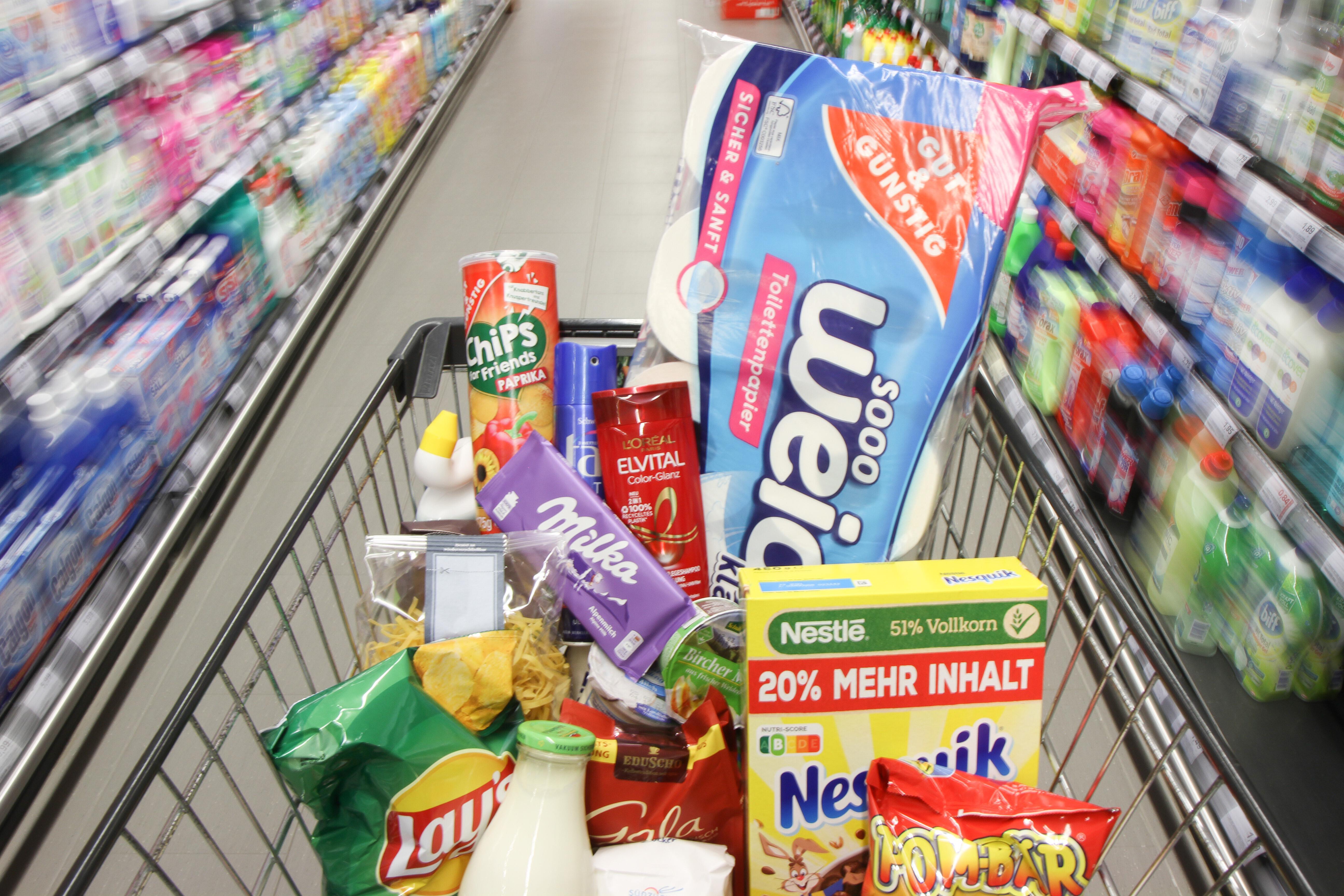 Ein vollbeladener Einkaufswagen mit Produkten fährt durch die Gänge in einem Discounter. (Symbolbild)