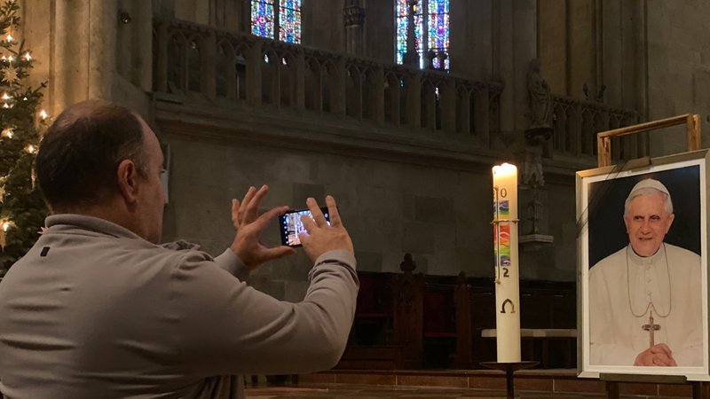 Ein Besucher im Regensburger Dom fotografiert ein Bild zum Gedenken an den verstorbenen emeritierten Papst Benedikt XVI im Regensburger Dom.