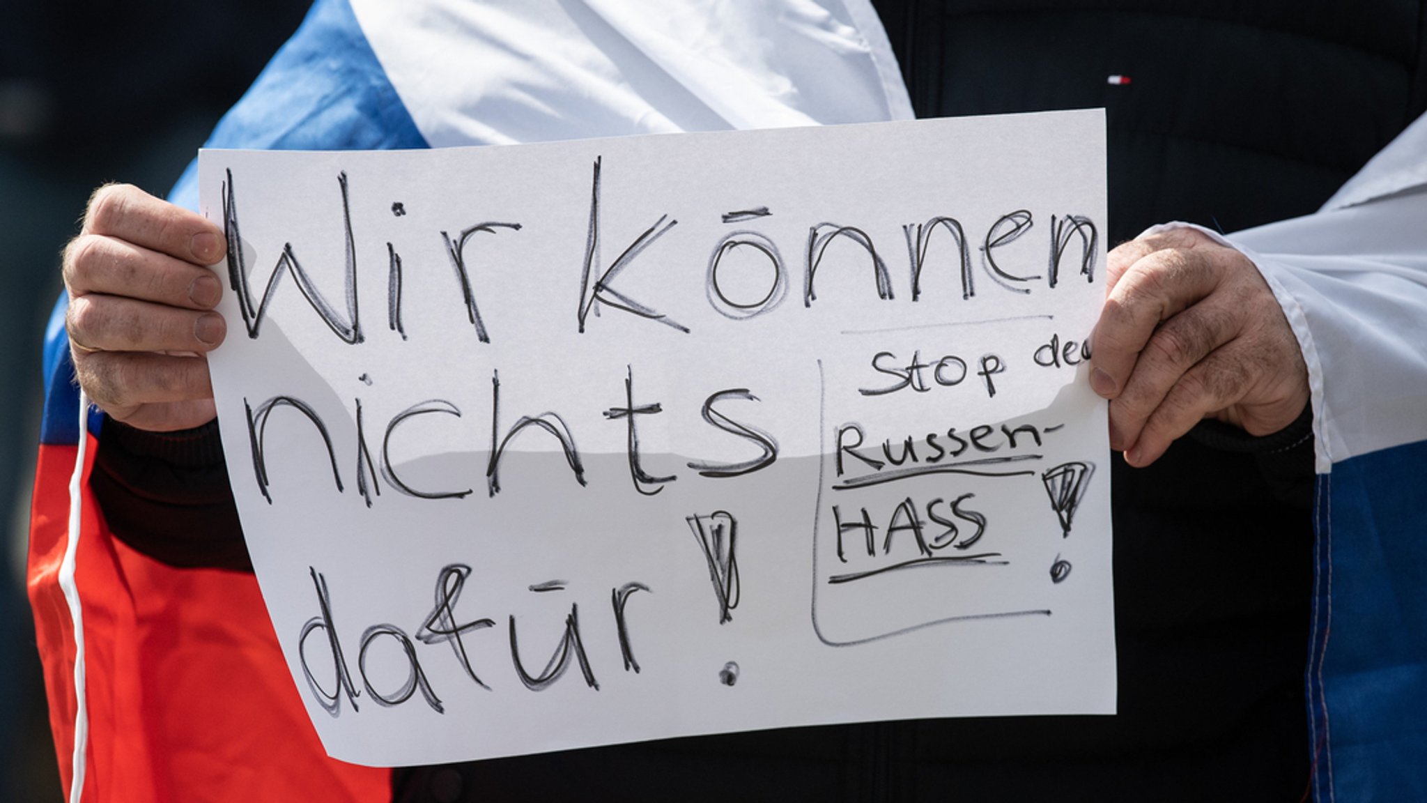 "Wir können nichts dafür - Stop den Russen-Hass"· steht auf dem Schild eines Mannes, der an einer prorussischen Kundgebung teilnimmt. 