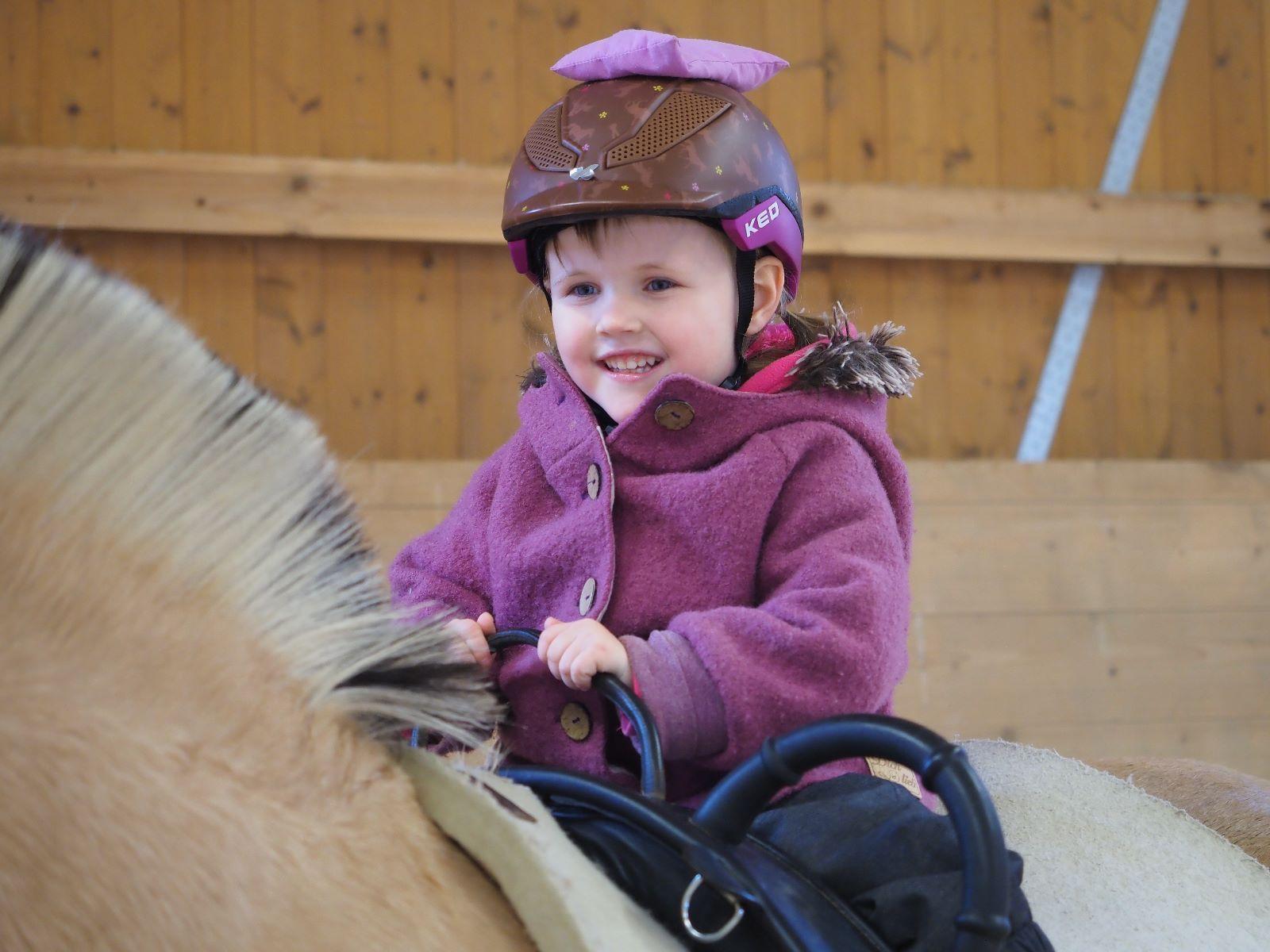Ein Mädchen sitzt lächelnd auf einem Norweger-Pony. 