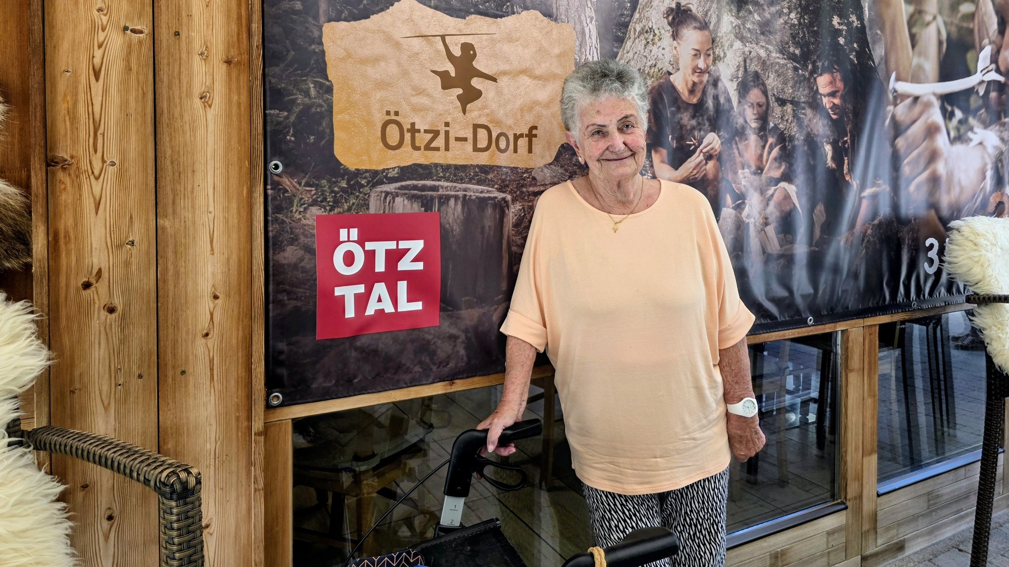 Ötzi-Finderin Erika Simon steht mit ihrem Rollator vor einer Fotowand im Ötzi-Dorf in Tirol. | Bild: BR/Ulrike Nikola Ötzi-Finderin Erika Simon steht mit ihrem Rollator vor einer Fotowand im Ötzi-Dorf in Tirol.