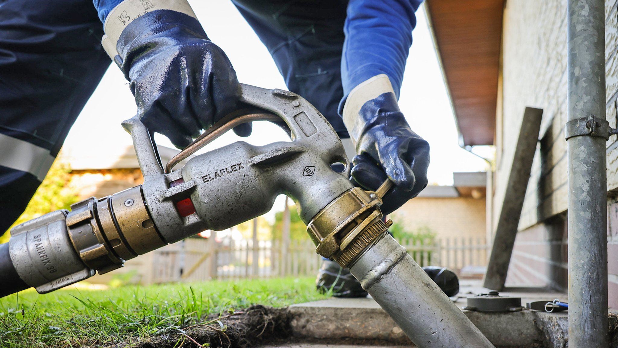 Ein Mitarbeiter eines Diesel- und Heizöl-Unternehmens verbindet einen Schlauch mit Zapfpistole an einen Füllstutzen für die Heizöllieferung an einen Kunden in einem Einfamilienhaus.