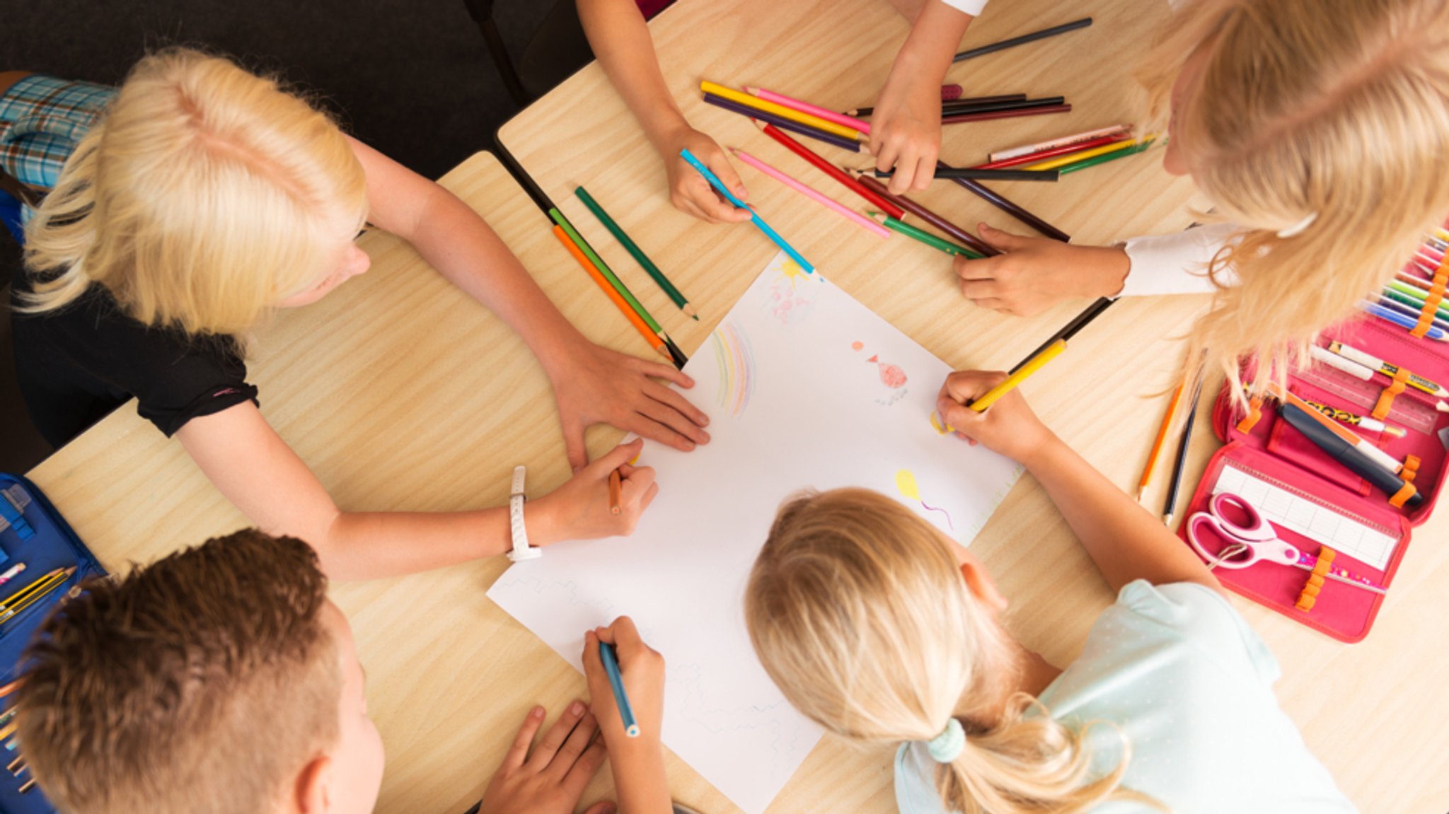 (Symbolbild) Kinder beugen sich zusammen über ein Blatt Papier und malen mit Buntstiften ein Bild.