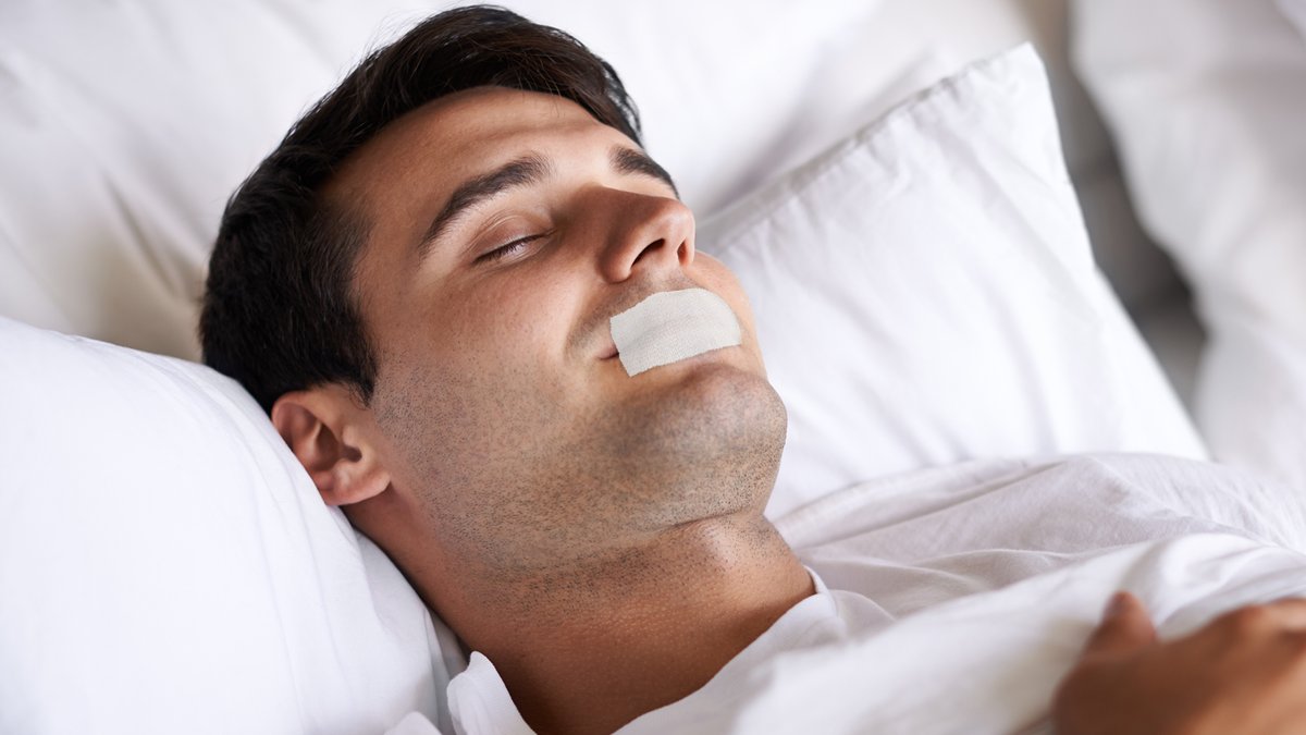 Mann liegt mit zugeklebtem Mund im Bett