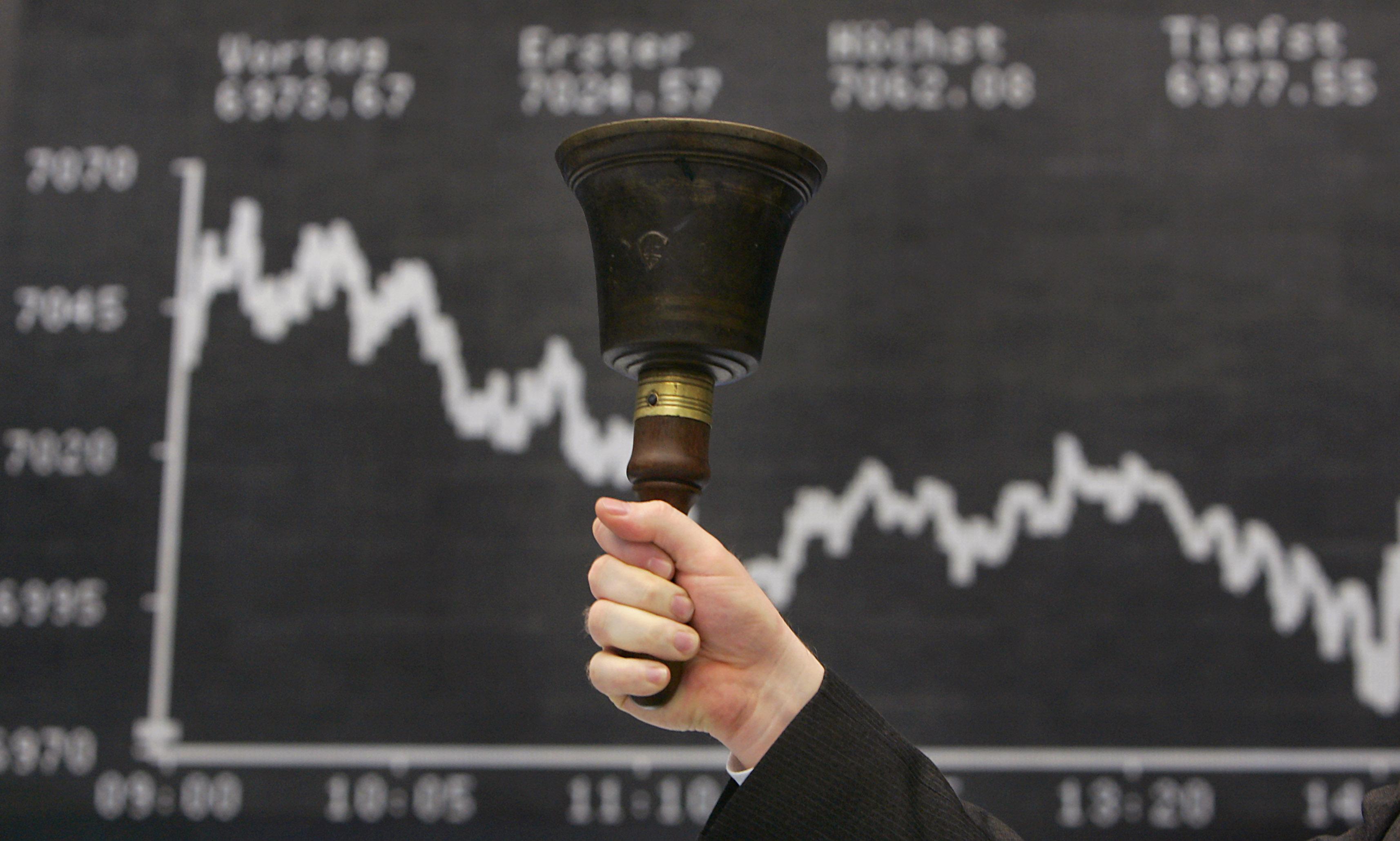 Symbolbild: Ein Mann hält eine Glocke vor der Anzeigentafel des Deutschen Aktien Index (DAX).