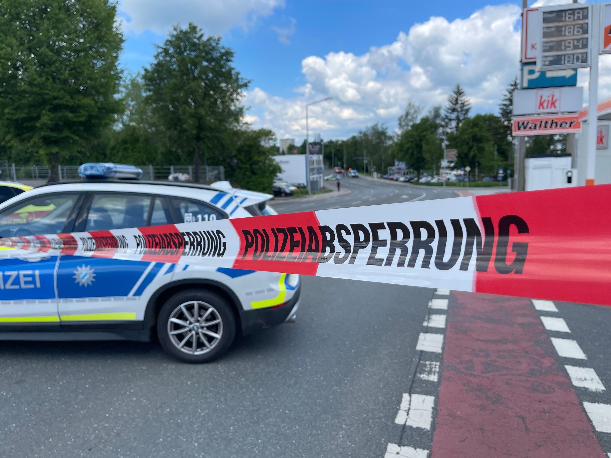 Ein Polizeiauto parkt quer zur Fahrbahn, davor ein weiß-rotes Band mit der Aufschrift "Polizeiabsperrung". 