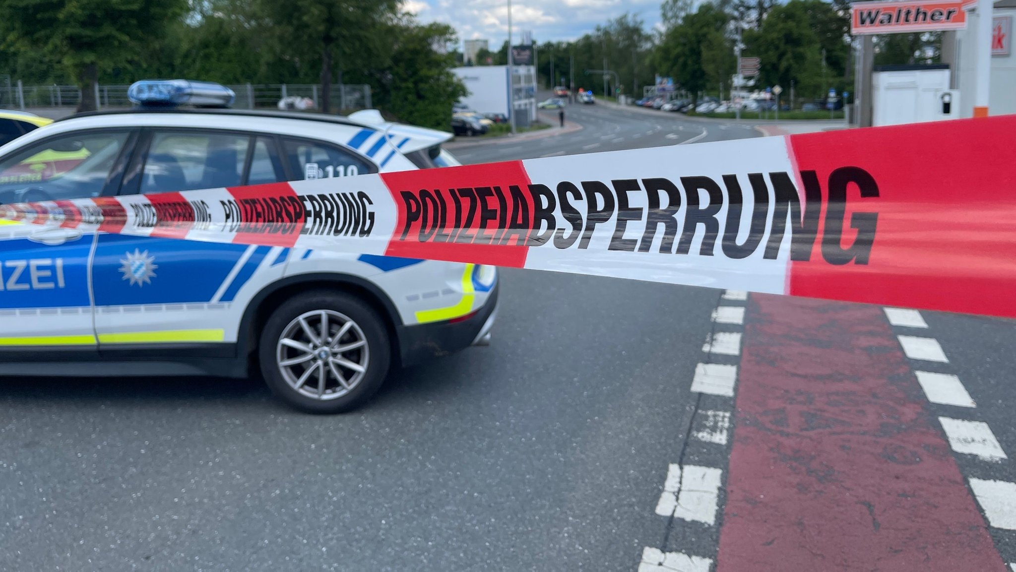 Ein Polizeiauto parkt quer zur Fahrbahn, davor ein weiß-rotes Band mit der Aufschrift "Polizeiabsperrung". 