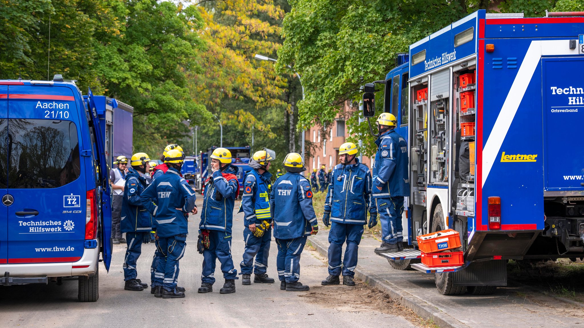 Mitarbeiter des THW stehen bei einer Übung neben ihren Fahrzeugen