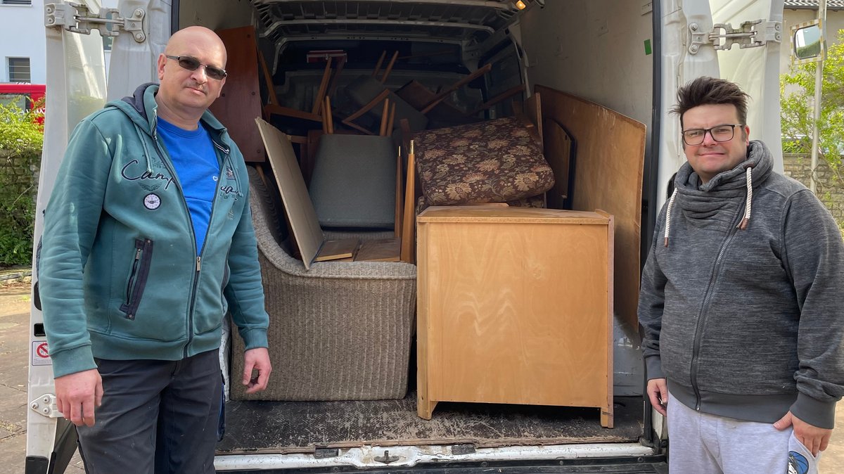 Zwei Männern vor Möbeln in einem Kasdtenwagen.