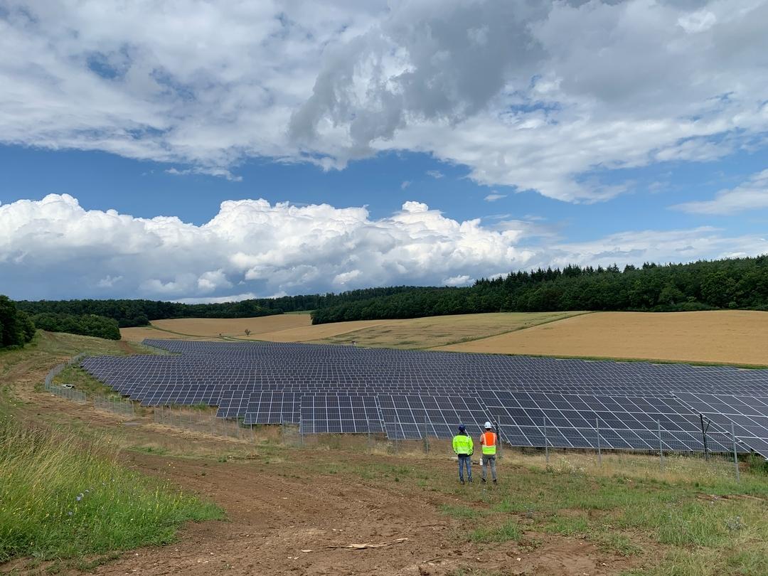 Zwei Arbeiter in Warnwesten stehen vor einem Solarpark auf einem Feld.